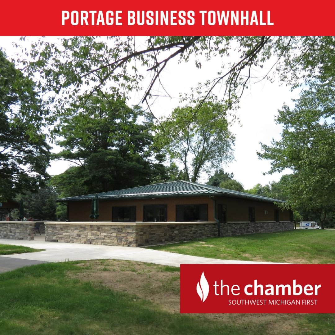 photo of the public building at Portage Shrier Park. It's a stone building with columns with a metal green roof. There is a sidewalk in front surrounded by green grass.